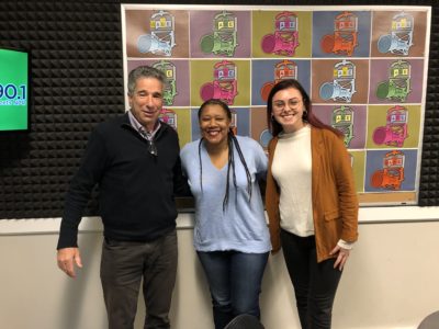 Larry Schall, Rose, Scott, and Makayla Adams standing against colorful WABE radio station logos on wall